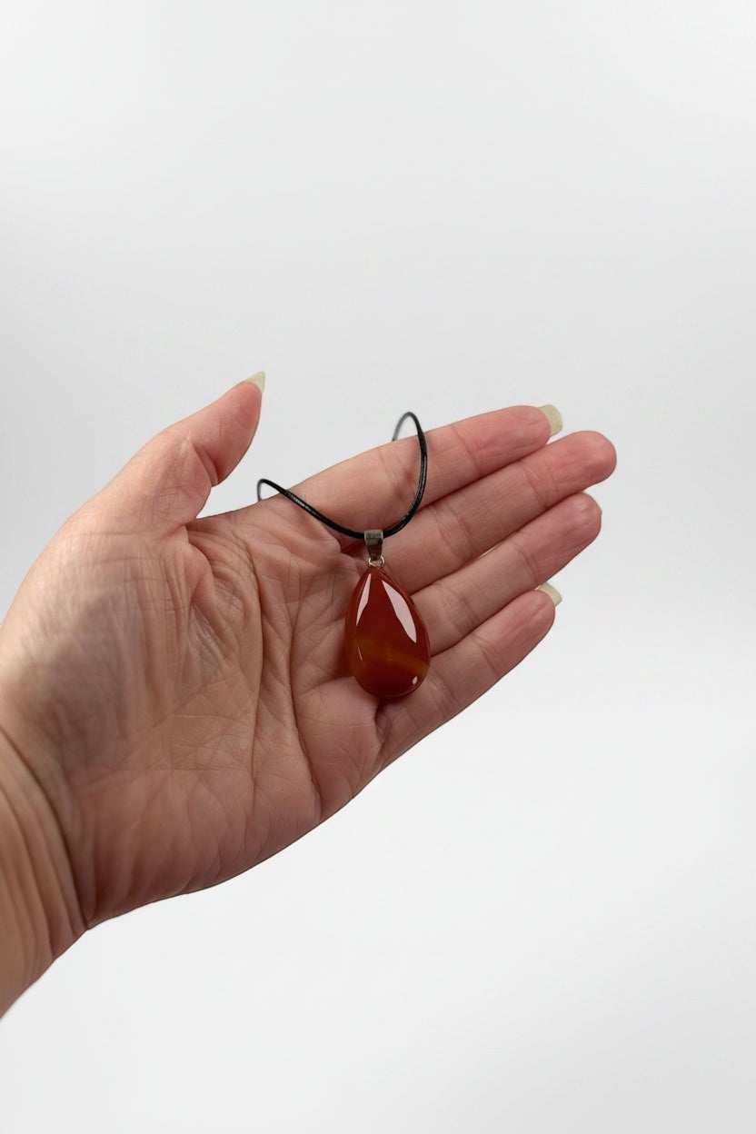 Treasured Energies carnelian teardrop pendant necklace held in a palm, featuring a polished orange-red gemstone.