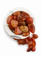 Treasured Energies polished carnelian stone tumbled gemstones in a white marble bowl on a white background.