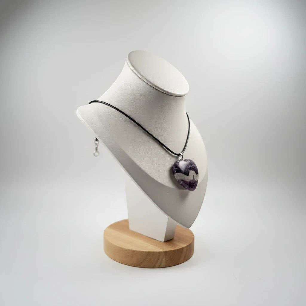 Treasured Energies heart-shaped chevron amethyst pendant on a black cord necklace displayed on a white bust stand.