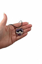 Treasured Energies heart-shaped chevron amethyst pendant necklace with purple and white bands held in a hand