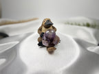 Treasured Energies Chevron Amethyst heart crystal held by a small carved wooden platypus figurine on white fabric.