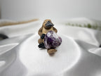 Treasured Energies heart-shaped Chevron Amethyst crystal held by a small platypus figurine on white satin fabric.