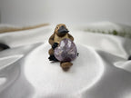 Treasured Energies heart-shaped Chevron Amethyst crystal held by a small platypus figurine on white satin fabric.