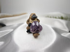 Treasured Energies Chevron Amethyst heart crystal held by a small platypus figurine on a white satin background.
