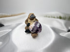 Treasured Energies heart-shaped Chevron Amethyst crystal held by a small platypus figurine on white satin fabric.