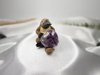 Treasured Energies heart-shaped Chevron Amethyst crystal held by a small platypus figurine on a white satin fabric