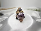 Treasured Energies Chevron Amethyst heart crystal held by a small platypus figurine on a white satin background.