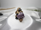 Treasured Energies Chevron Amethyst heart crystal held by a small platypus figurine on a white satin fabric background.