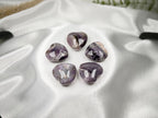 Treasured Energies Chevron Amethyst heart-shaped crystals with purple and white bands on a white satin fabric.