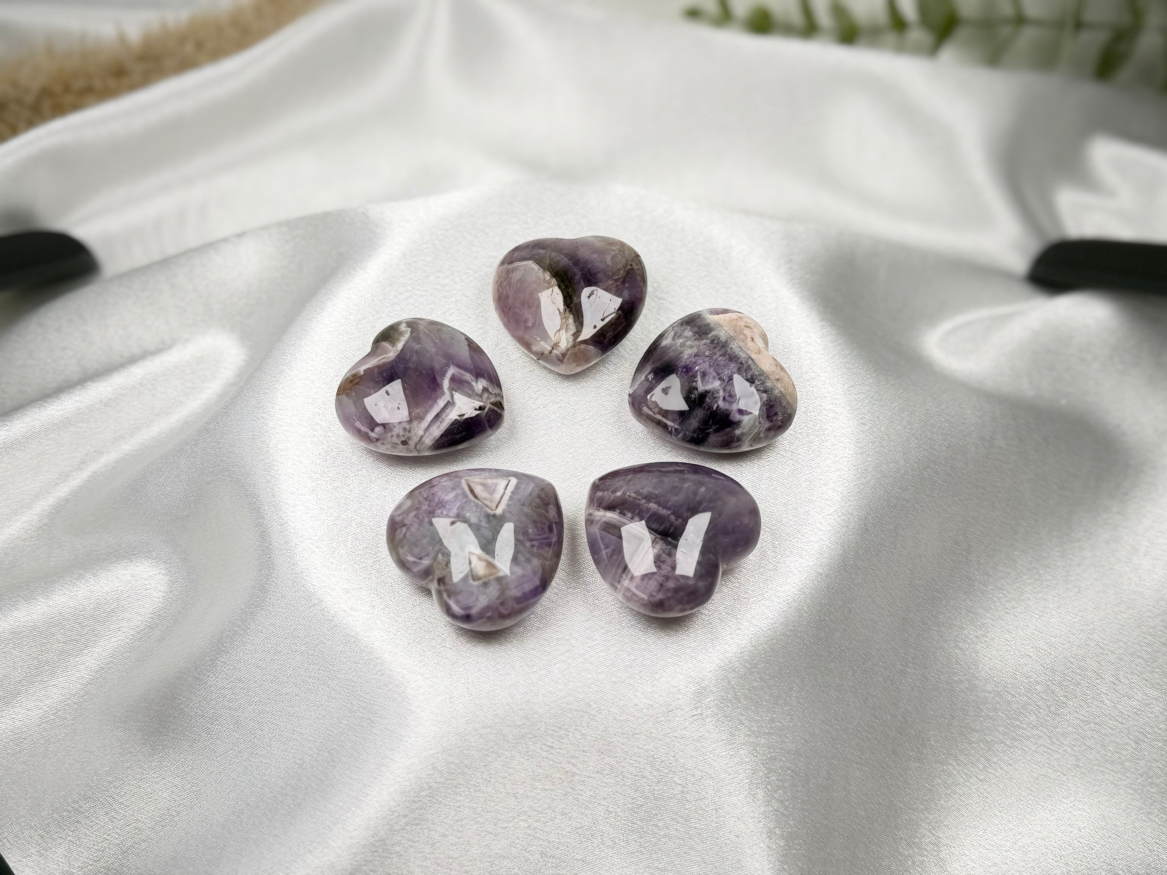 Treasured Energies Chevron Amethyst heart-shaped crystals with purple and white bands on a white satin fabric.