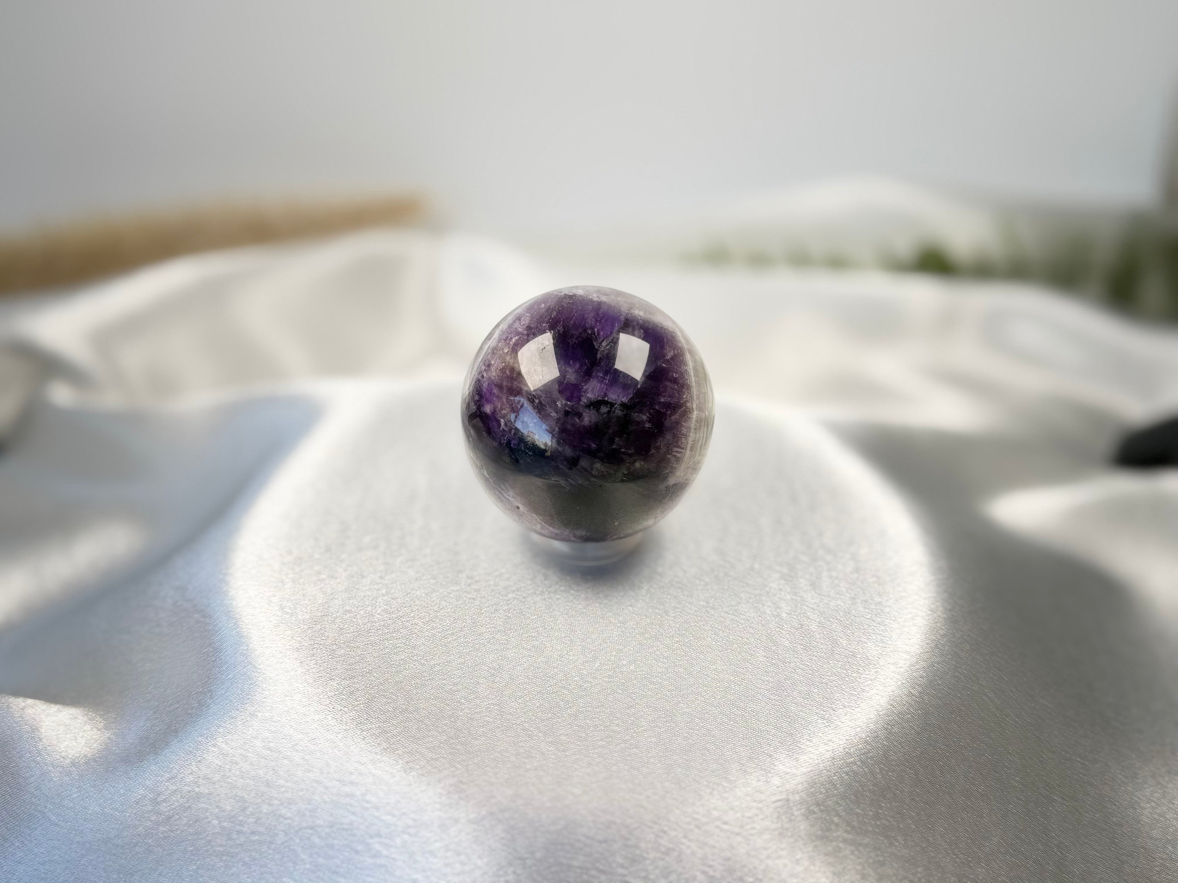 Treasured Energies polished chevron amethyst crystal sphere with purple and white bands on a white satin cloth
