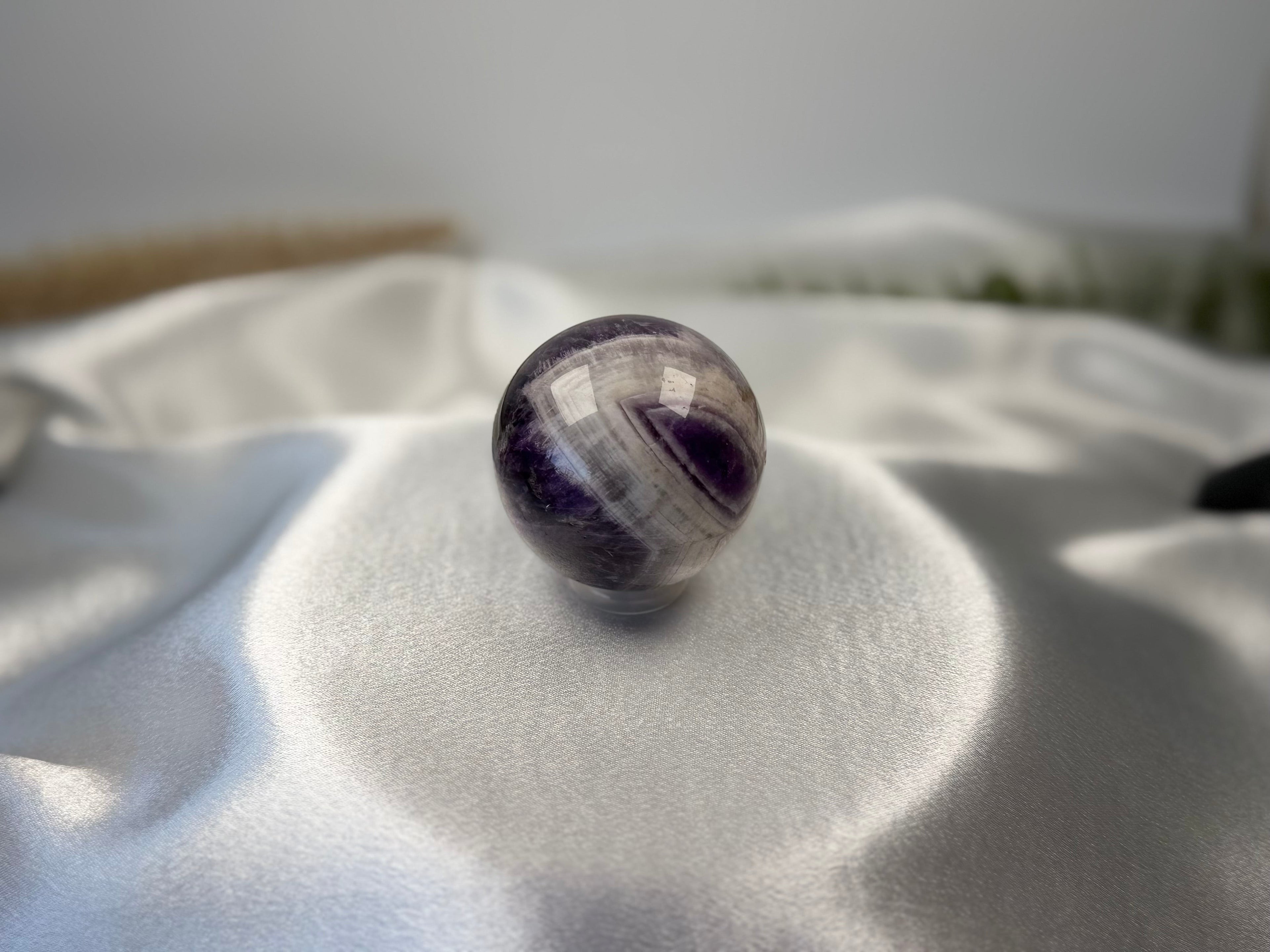 Treasured Energies polished Chevron Amethyst crystal sphere featuring deep purple and white V-shaped bands on satin.
