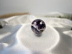 Treasured Energies polished Chevron Amethyst crystal sphere with deep purple and white V-shaped bands on white silk.