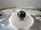 Treasured Energies polished Chevron Amethyst crystal sphere with purple and white V-shaped bands on white satin fabric