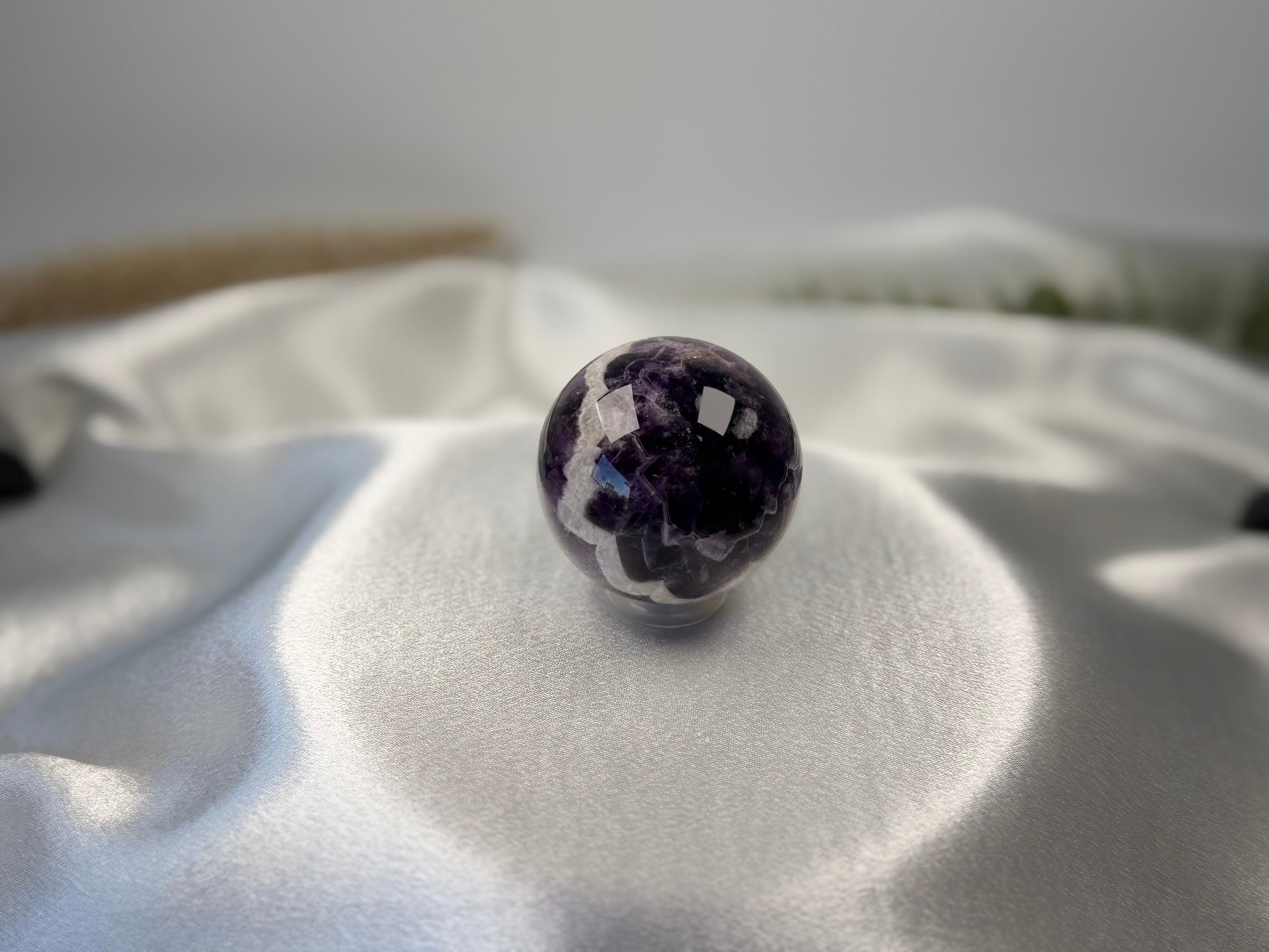 Treasured Energies polished Chevron Amethyst crystal sphere with purple and white V-shaped bands on white satin fabric