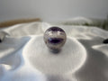 Treasured Energies polished Chevron Amethyst crystal sphere with deep purple and white V-shaped bands on satin fabric.