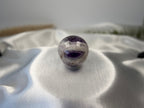 Treasured Energies polished Chevron Amethyst crystal sphere with deep purple and white V-shaped bands on satin fabric.