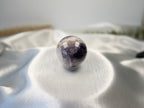 Treasured Energies polished Chevron Amethyst crystal sphere with purple and white V-shaped bands on white silk fabric.