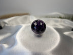 Treasured Energies polished Chevron Amethyst crystal sphere with deep purple and white V-shaped bands on satin fabric.