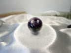 Treasured Energies polished Chevron Amethyst crystal sphere with deep purple and white bands on a white satin cloth.