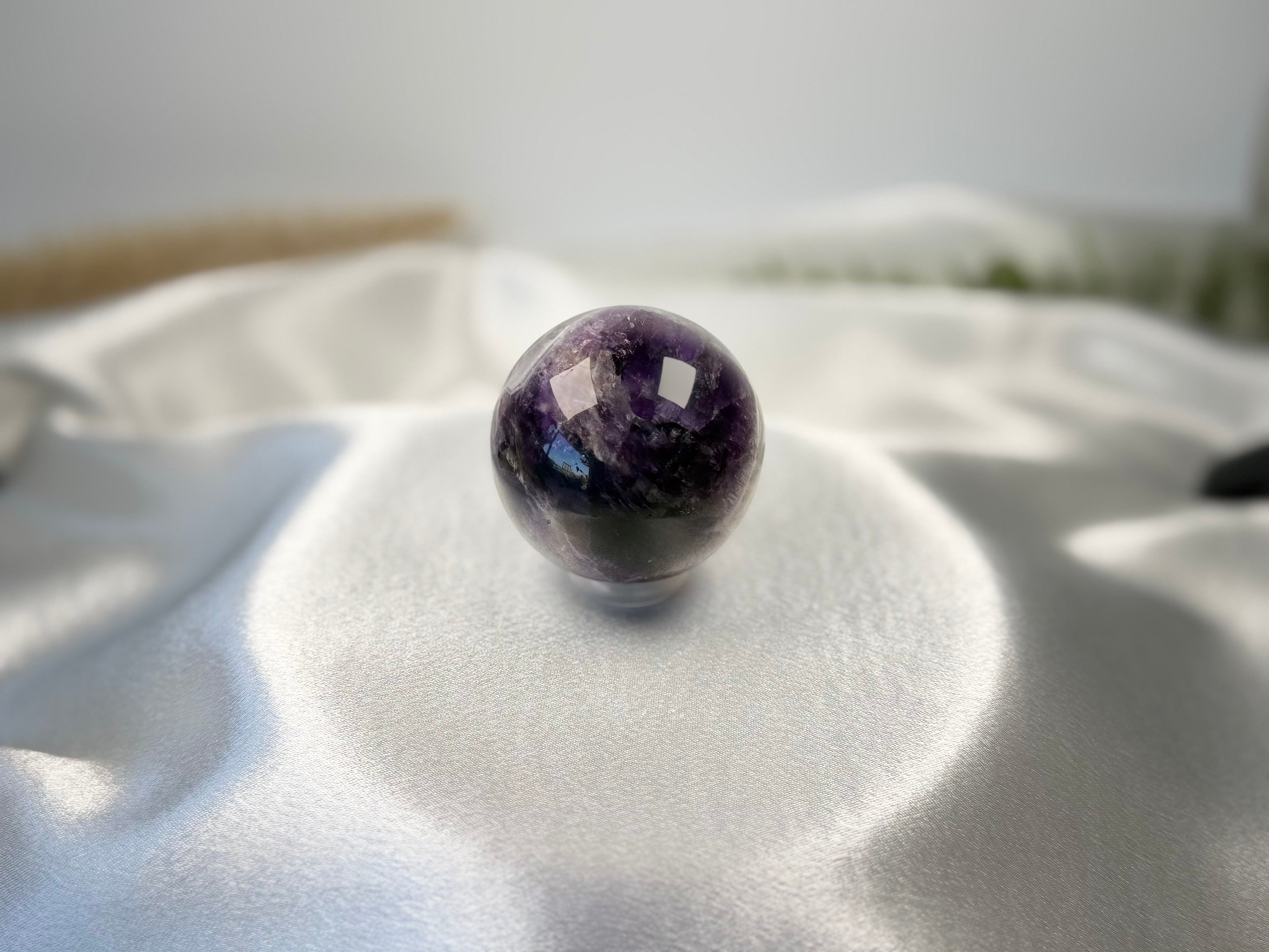 Treasured Energies polished Chevron Amethyst crystal sphere with deep purple and white bands on a white satin cloth.