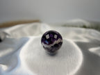 Treasured Energies polished chevron amethyst crystal sphere with deep purple and white V-shaped bands on satin fabric.