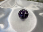 Treasured Energies polished Chevron Amethyst crystal sphere with deep purple and white V-shaped bands on satin fabric.