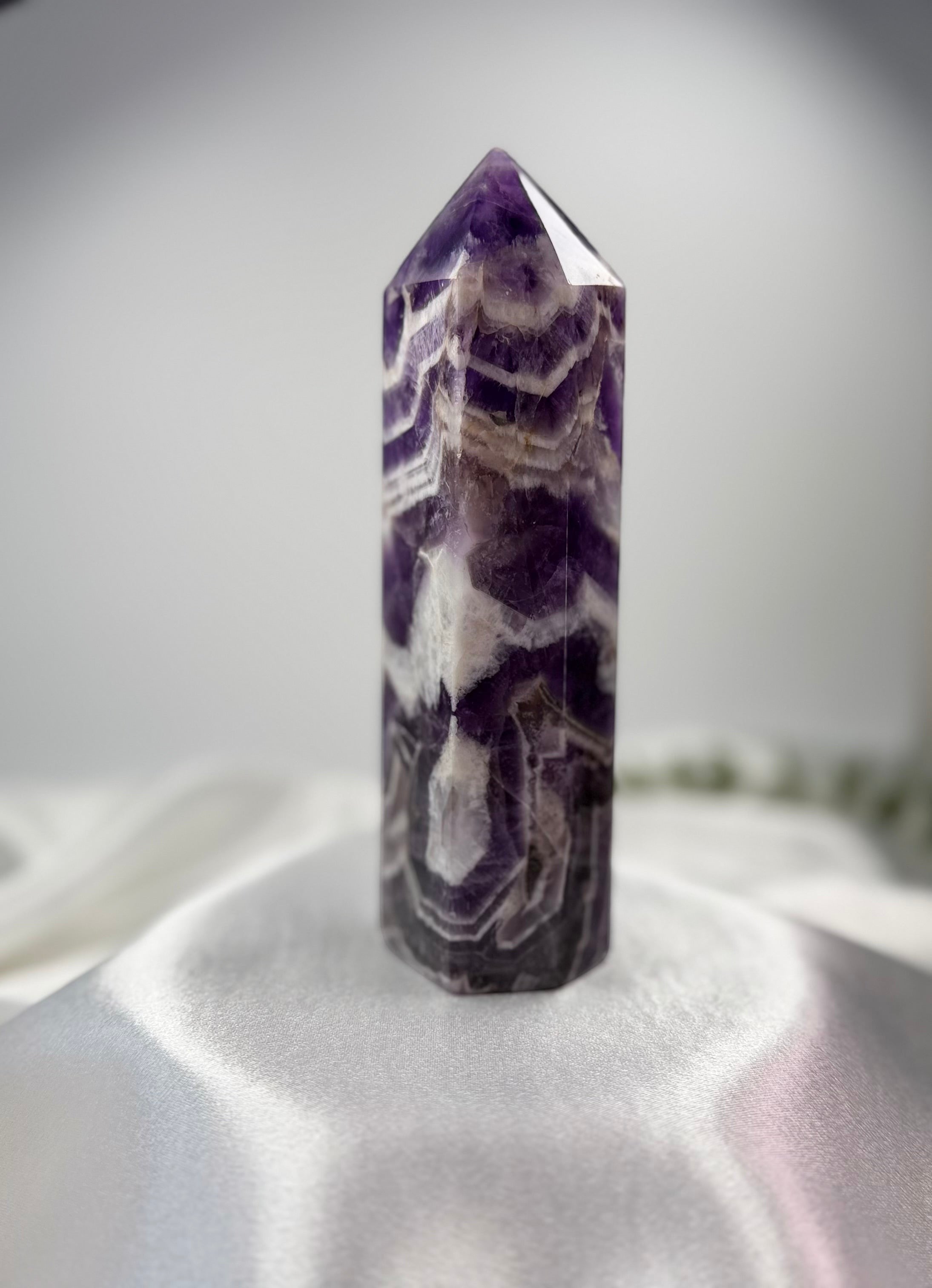 Treasured Energies Chevron Amethyst crystal tower with deep purple and milky white V-shaped bands on a white cloth.