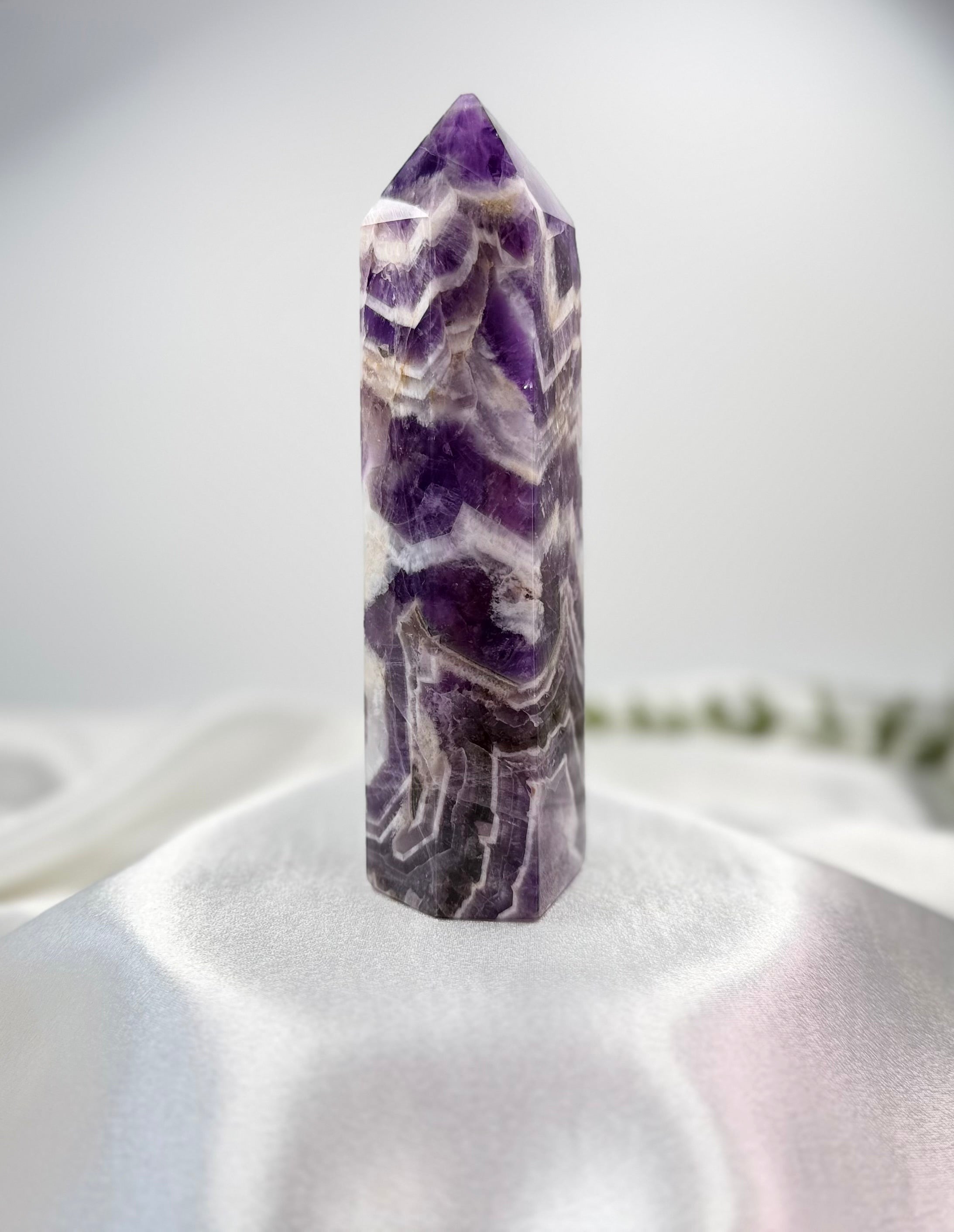 Treasured Energies Chevron Amethyst crystal tower with deep purple and white V-shaped bands on a white fabric base.