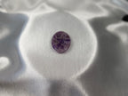 Treasured Energies Chevron Amethyst worry stone with purple and white V-shaped bands on a smooth white satin background.