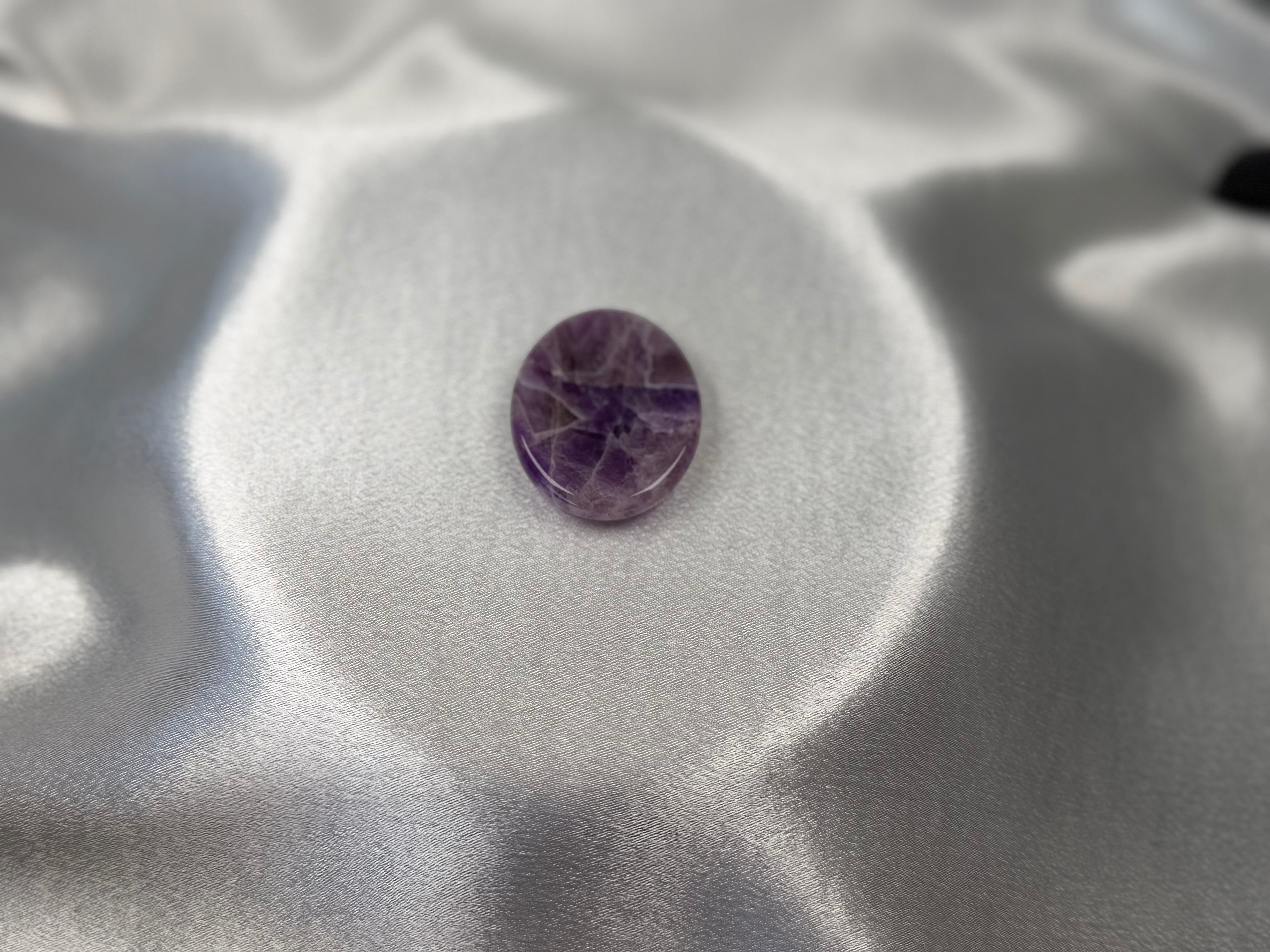 Treasured Energies Chevron Amethyst worry stone with purple and white V-shaped bands on a smooth white satin background.