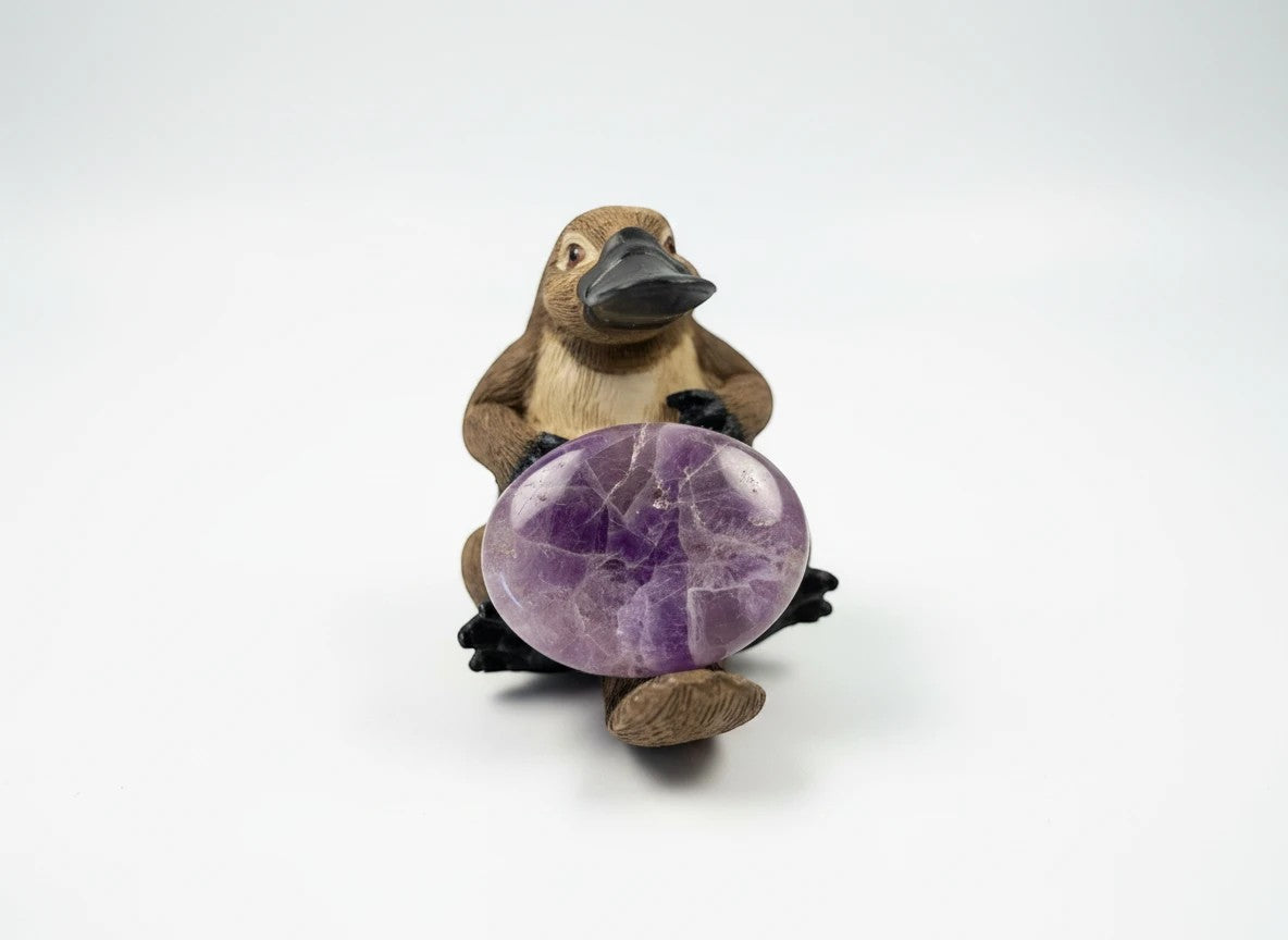 Treasured Energies Chevron Amethyst worry stone with purple and white bands held by a small platypus figurine.