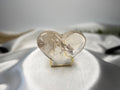 Treasured Energies clear quartz heart crystal with visible phantom inclusions on a gold display stand.
