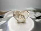 Treasured Energies clear quartz heart crystal with visible phantom inclusions on a gold display stand.