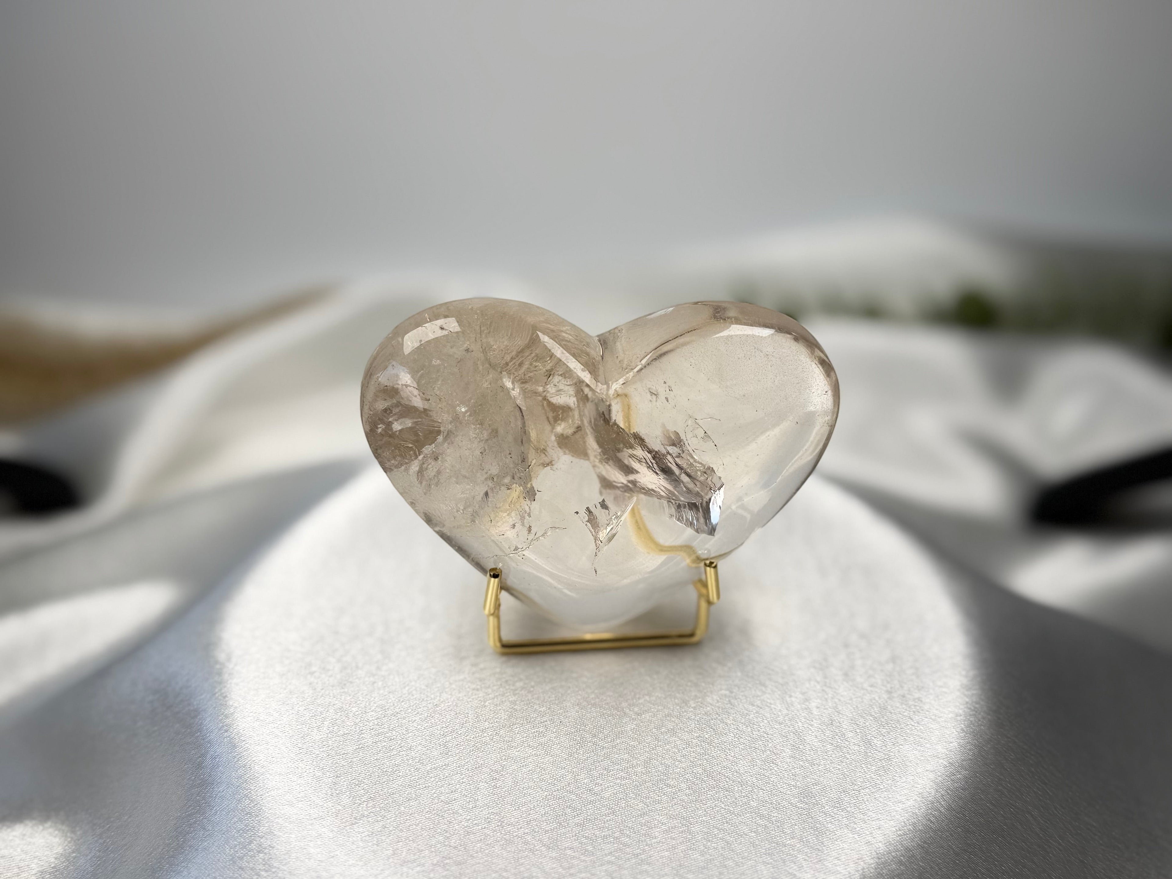Treasured Energies clear quartz heart crystal with visible phantom inclusions on a gold display stand.