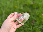 Treasured Energies clear quartz heart crystal with visible phantom inclusions held in a hand over a green lawn