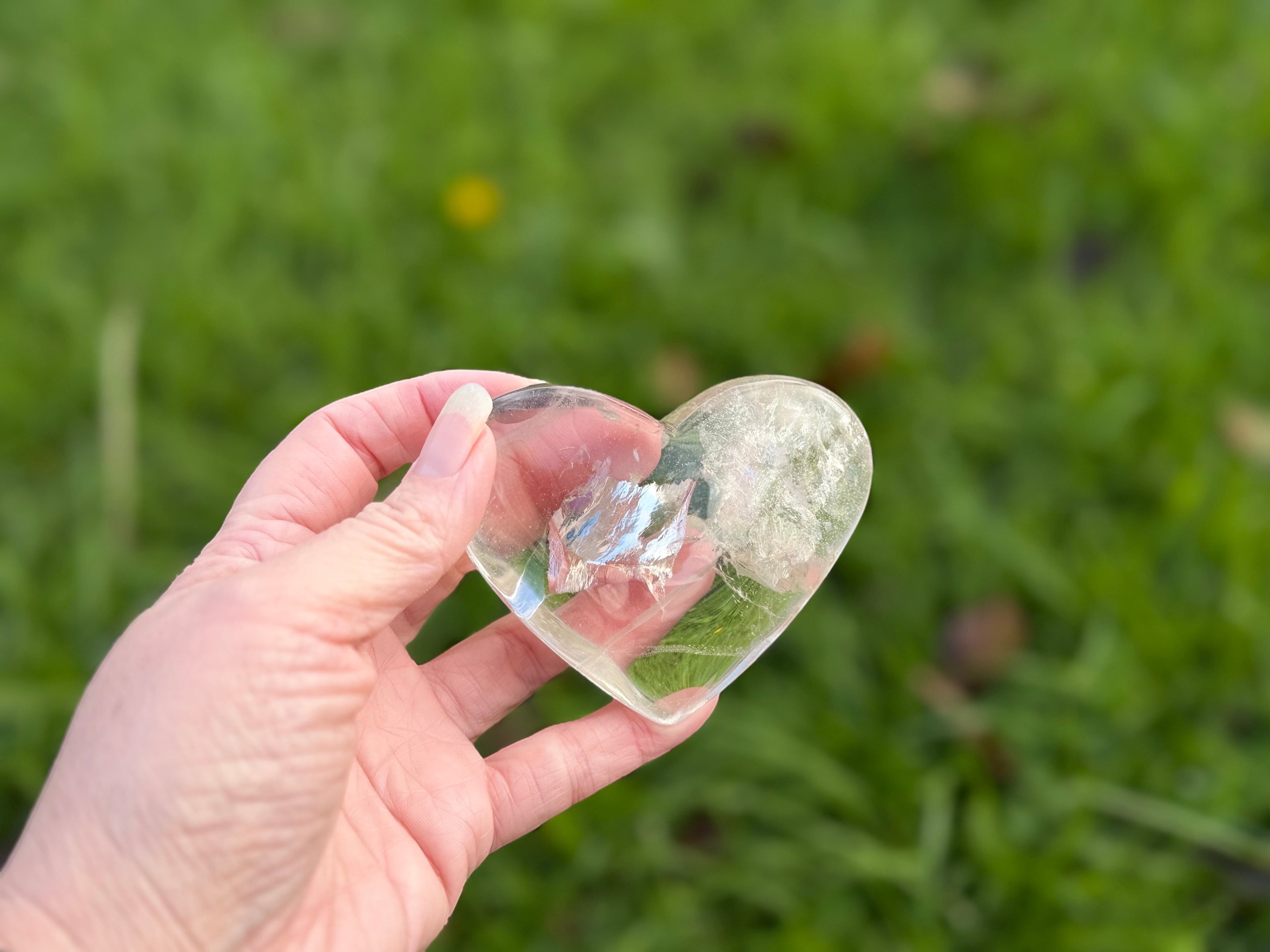 Treasured Energies clear quartz heart crystal with visible phantom inclusions held in a hand over a green lawn