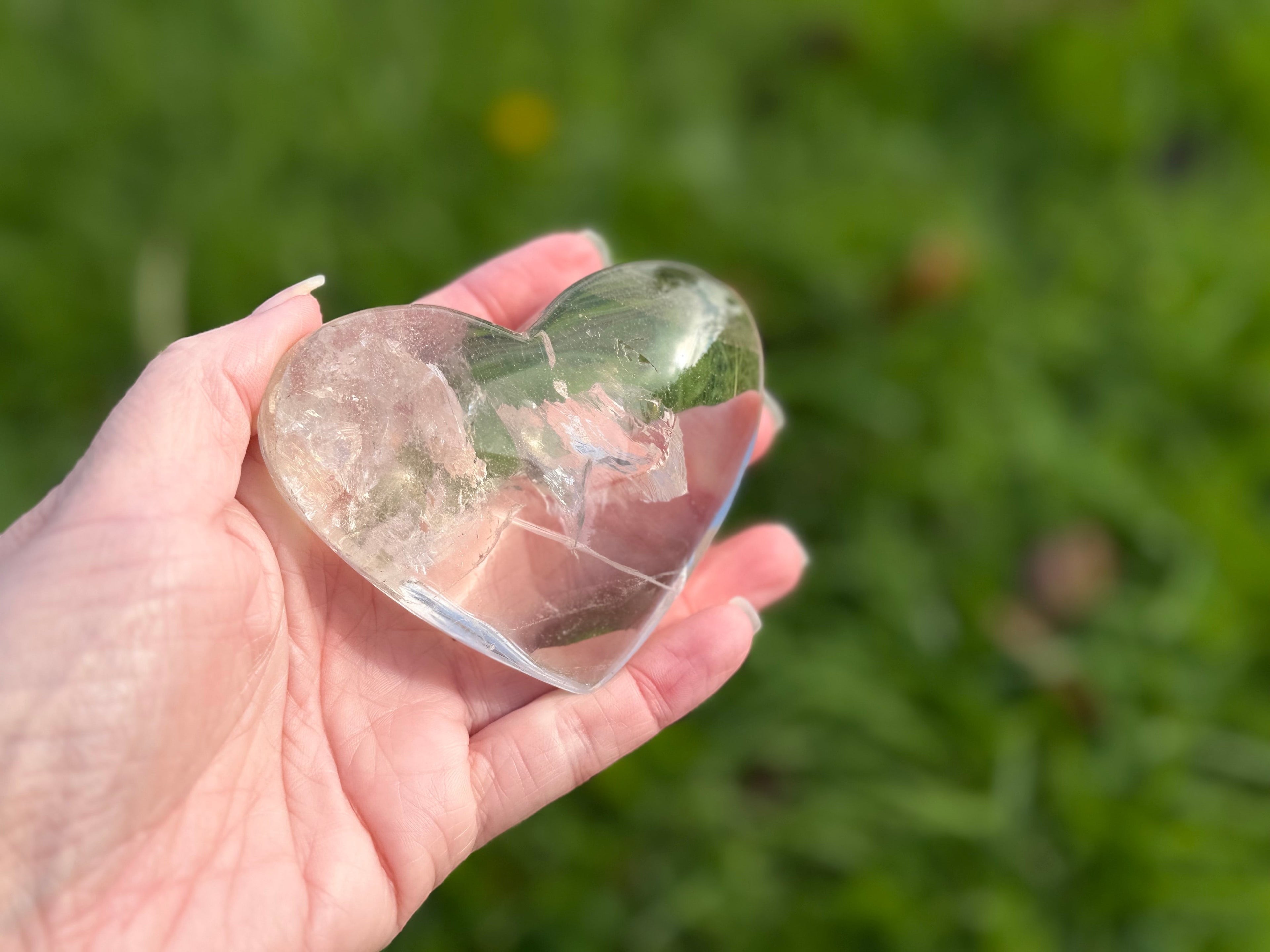 Treasured Energies clear quartz heart crystal with visible phantom inclusions held in a hand against a green background