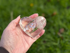 Treasured Energies clear quartz heart crystal with visible phantom inclusions held in a hand against a green background