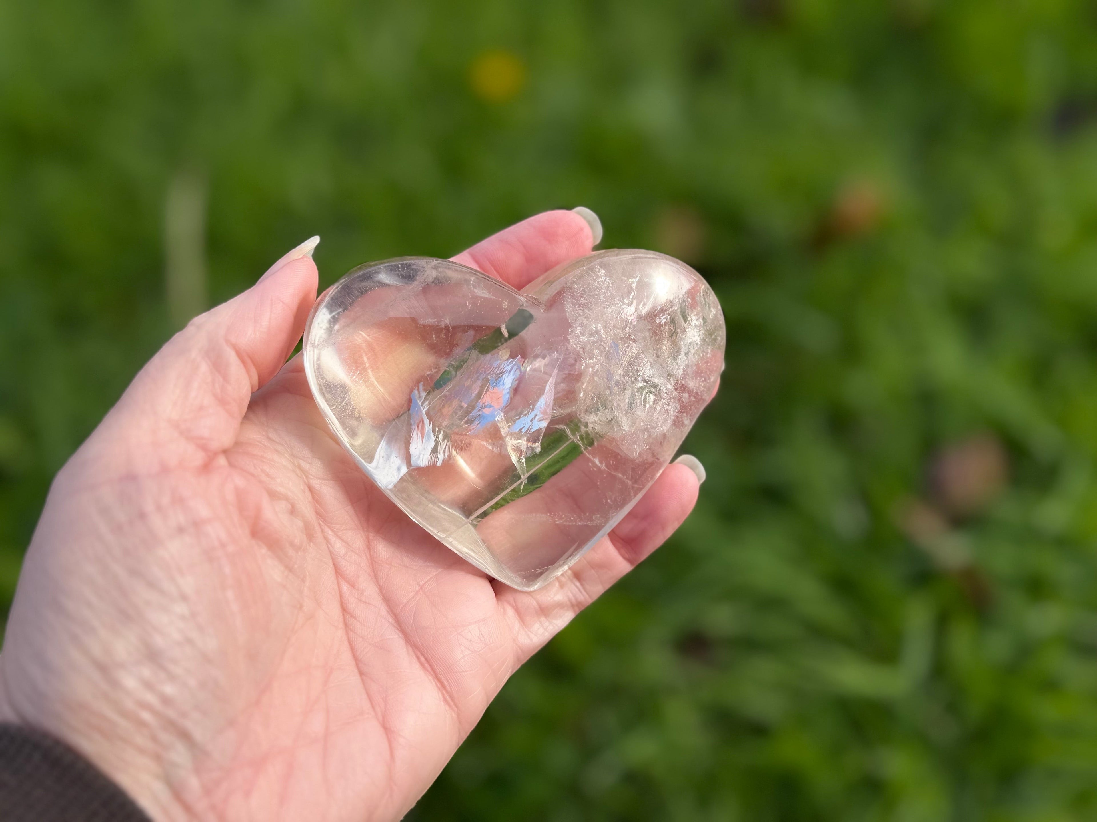 Treasured Energies clear quartz heart crystal with visible phantom inclusions held in a hand against a green background