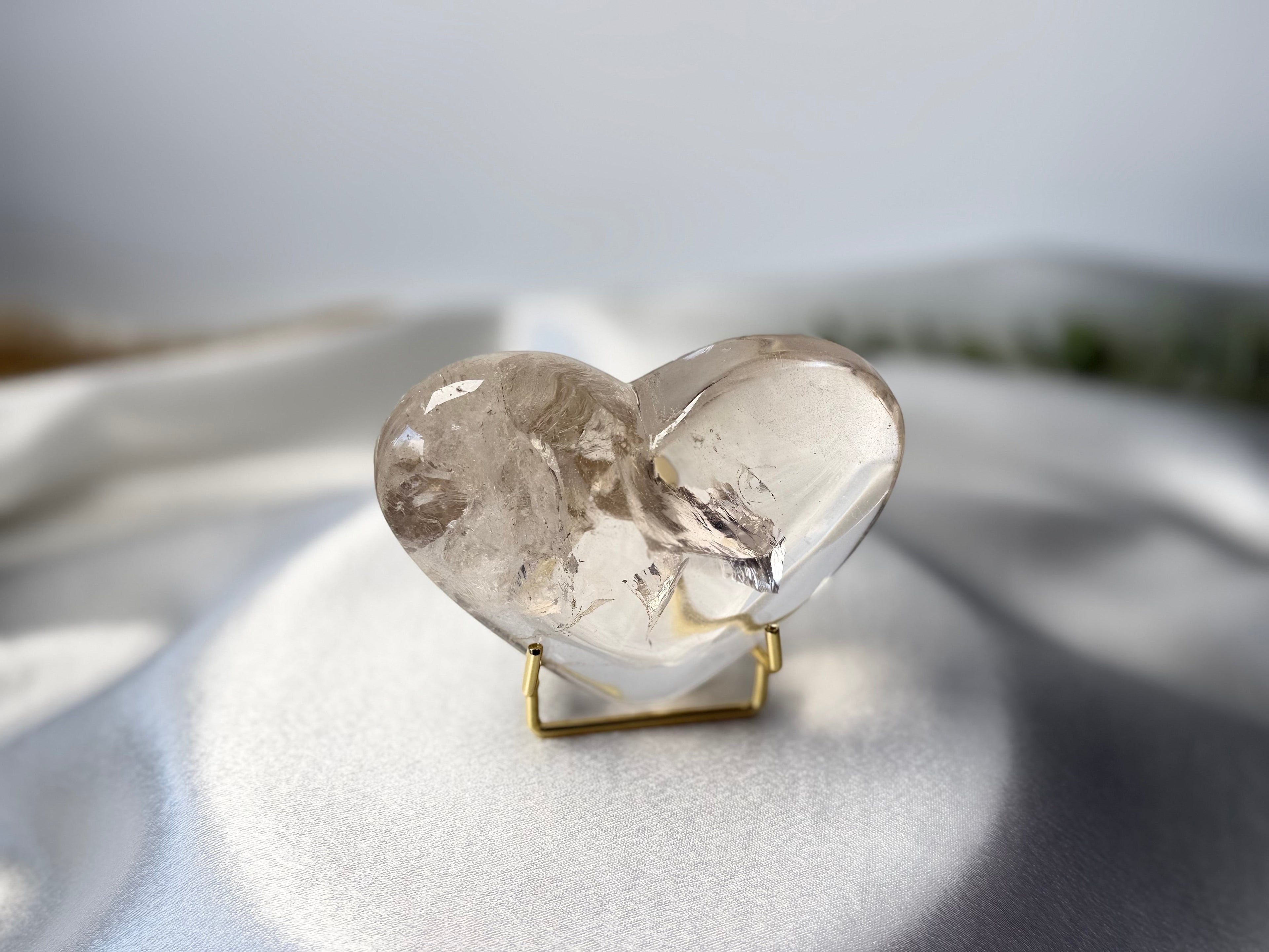 Treasured Energies clear quartz heart crystal with internal phantom inclusions on a gold display stand.