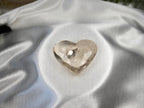 Treasured Energies clear quartz heart crystal with visible phantom inclusions resting on white satin fabric.