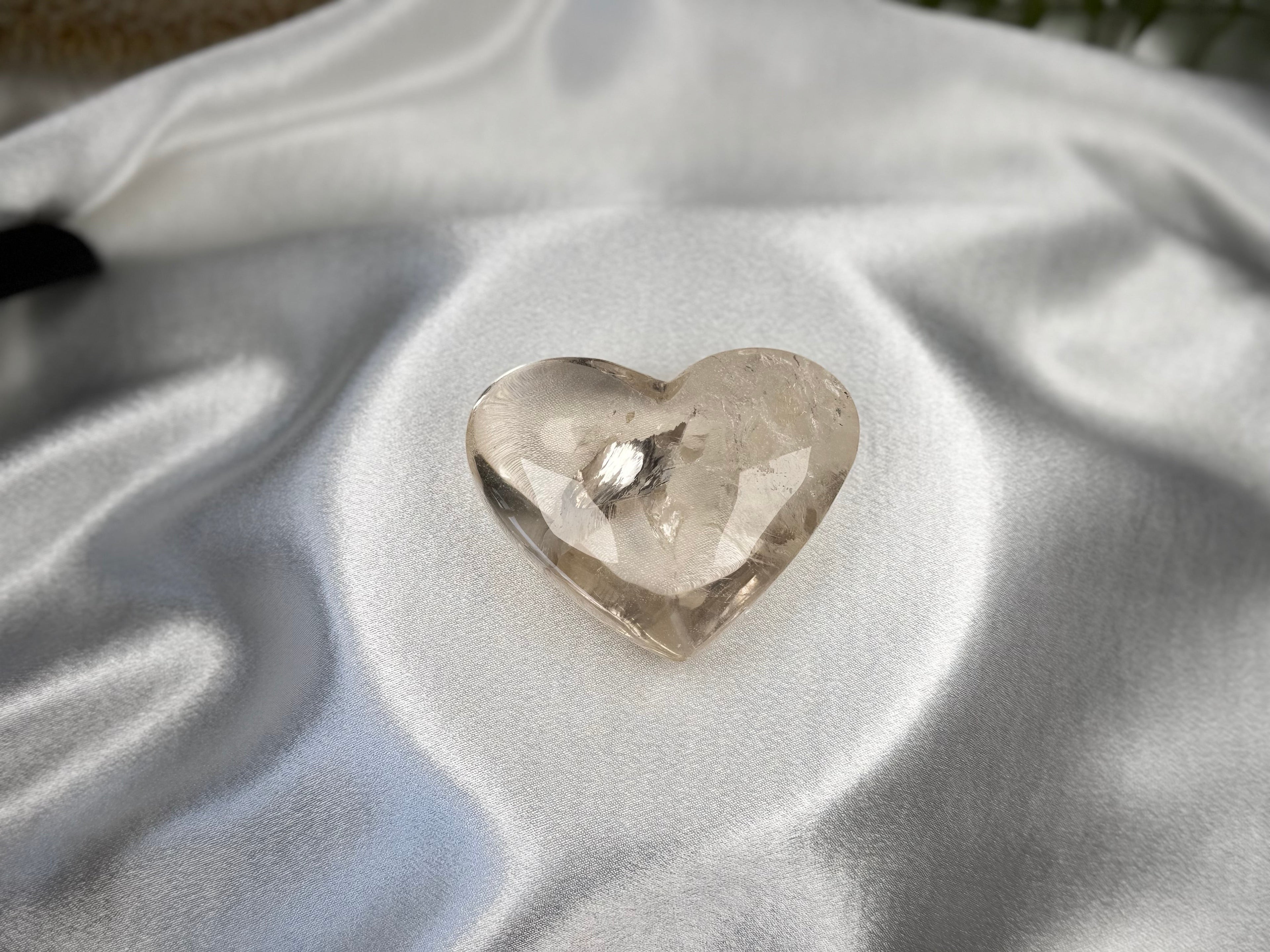 Treasured Energies clear quartz heart crystal with visible phantom inclusions resting on white satin fabric.