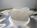 Treasured Energies clear quartz crystal tower with a raw, unpolished base and a smooth, faceted point on white silk.