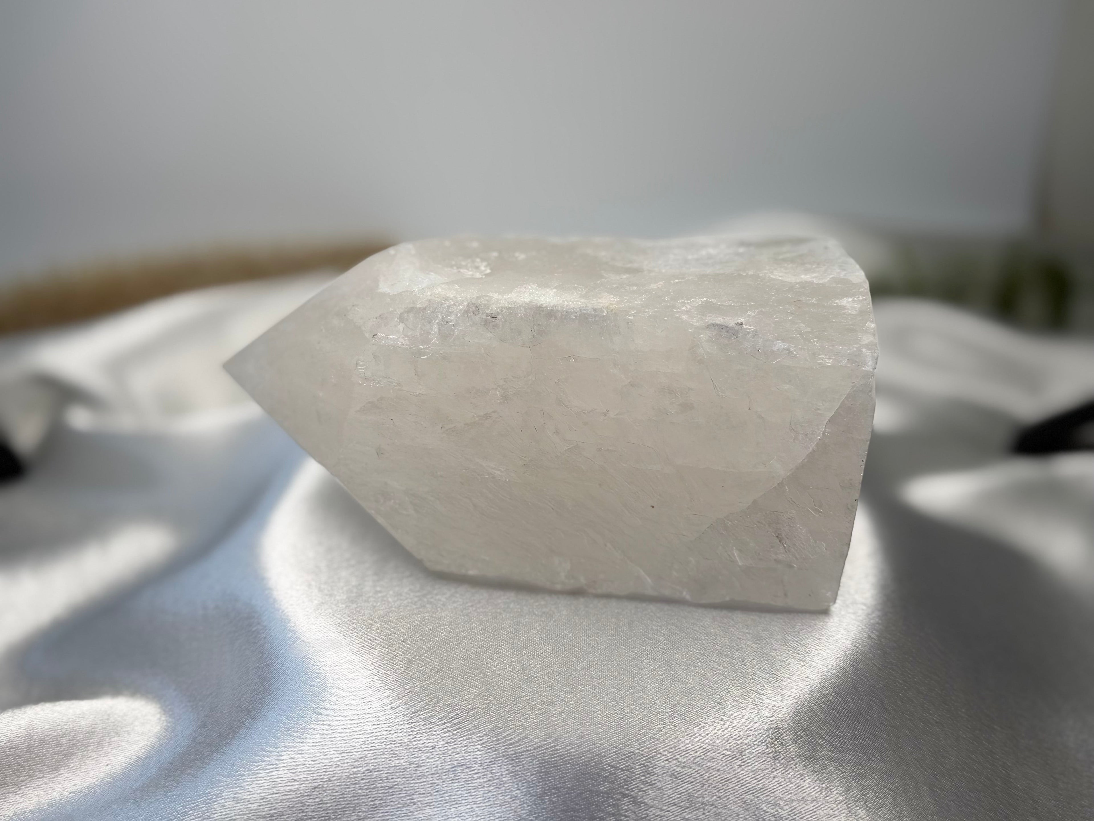 Treasured Energies clear quartz crystal tower with a raw, unpolished base and a smooth, faceted point on white silk.