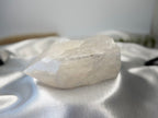 Treasured Energies clear quartz crystal point with a raw, unpolished base and a smooth, faceted top on white silk.
