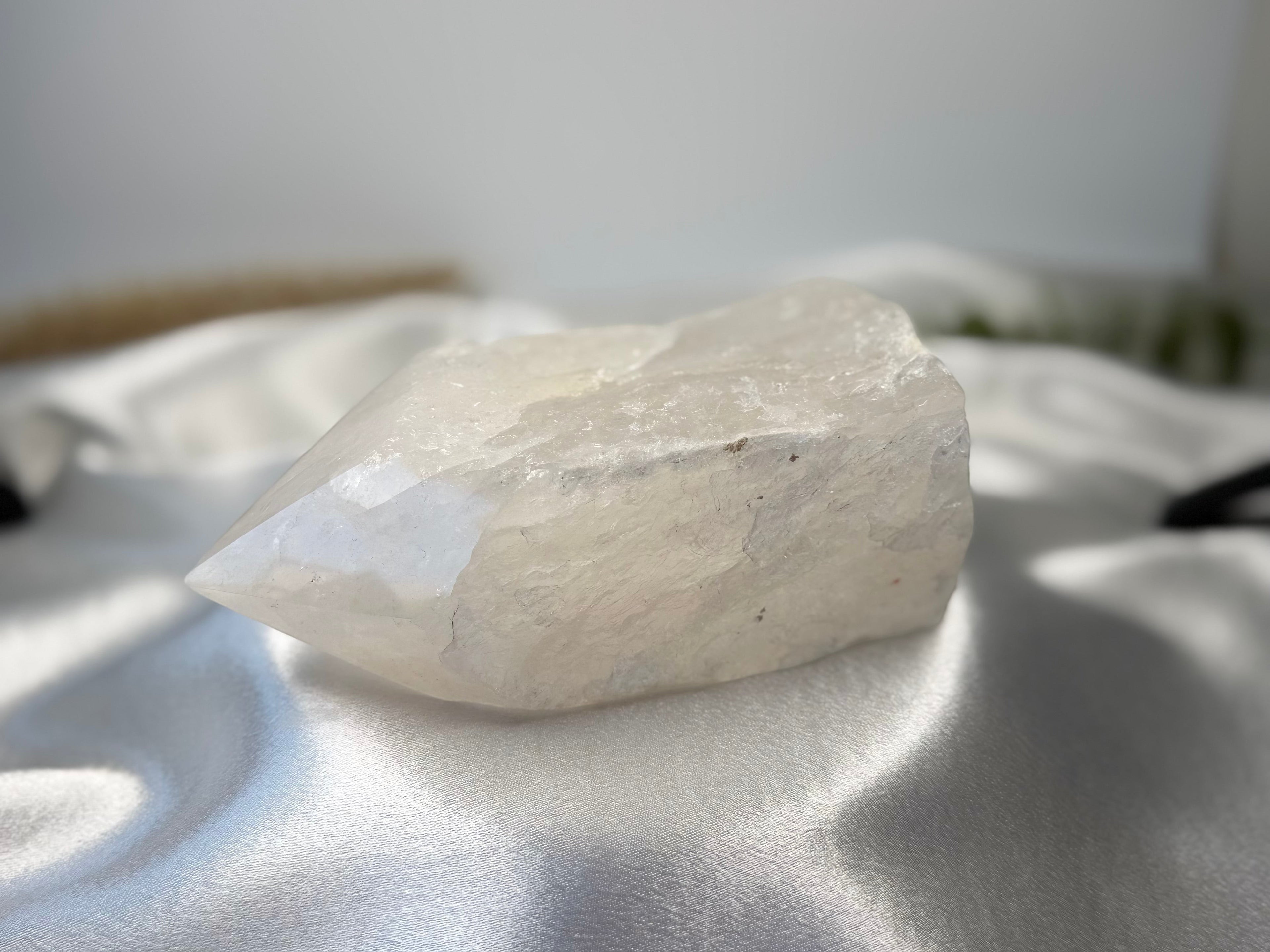 Treasured Energies clear quartz crystal point with a raw, unpolished base and a smooth, faceted top on white silk.