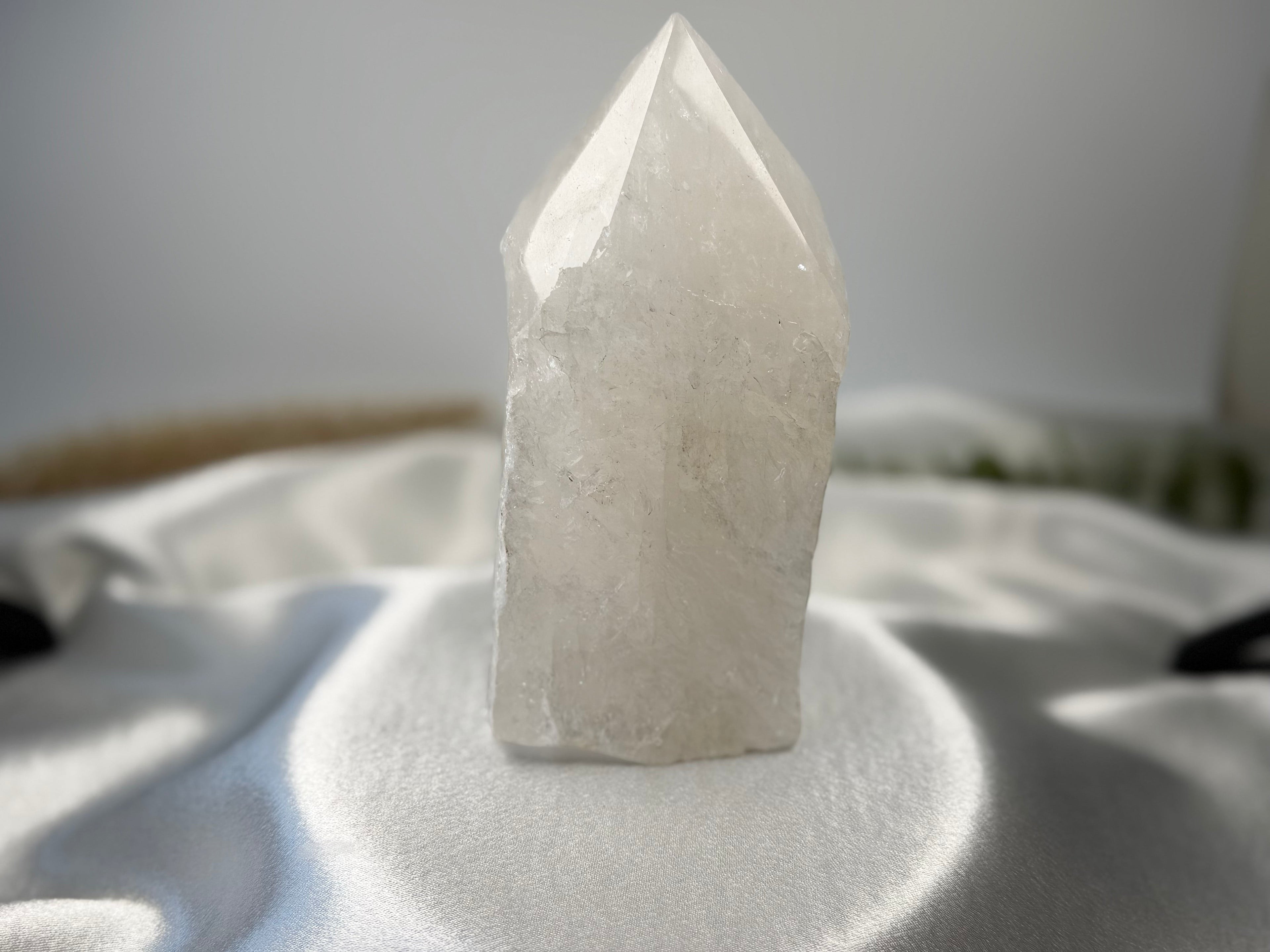 Treasured Energies clear quartz crystal tower with a raw base and polished faceted point on a white satin cloth.