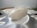 Treasured Energies clear quartz crystal tower with a polished point and raw base resting on white satin fabric