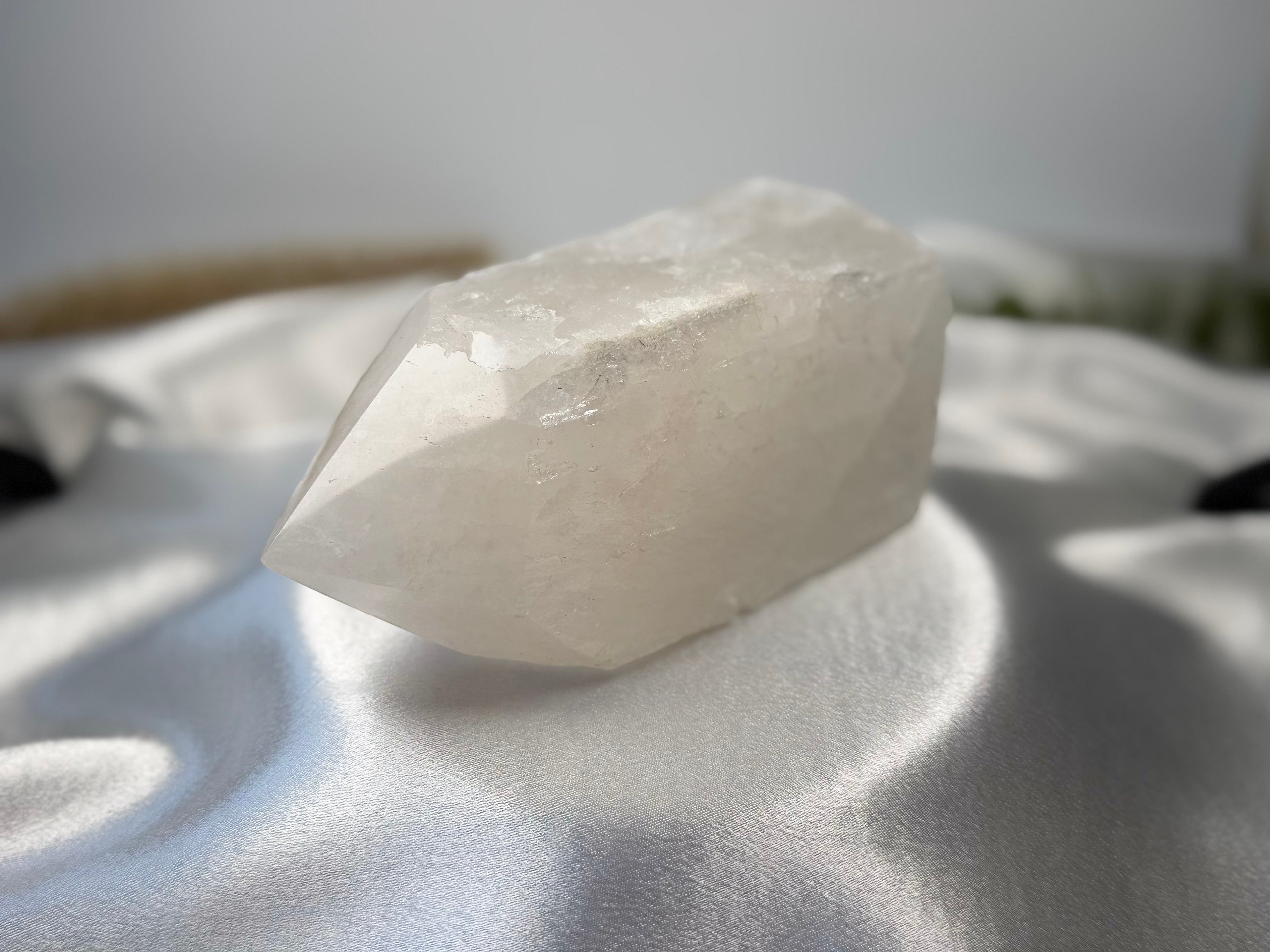 Treasured Energies clear quartz crystal tower with a polished point and raw base resting on white satin fabric